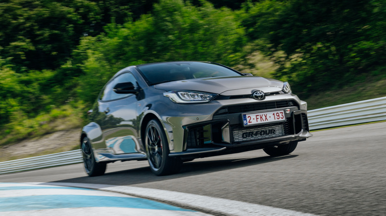 The facelifted Toyota GR Yaris in gray on a racetrack, front 3/4 view