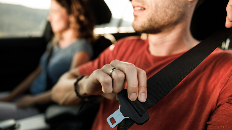 A driver putting on his seatbelt in a car.