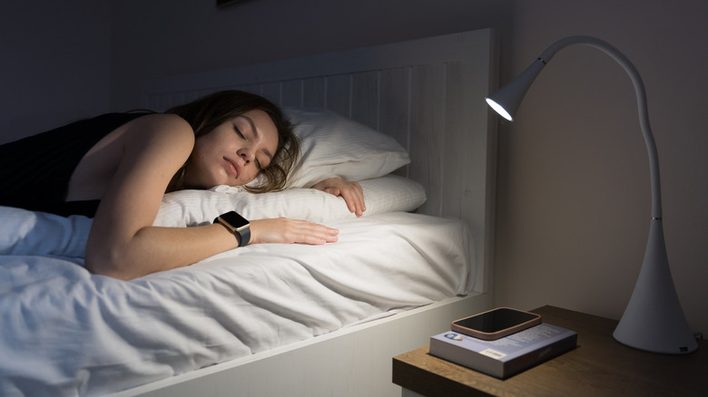 Women asleep on a bed with a lamp illuminated besider her