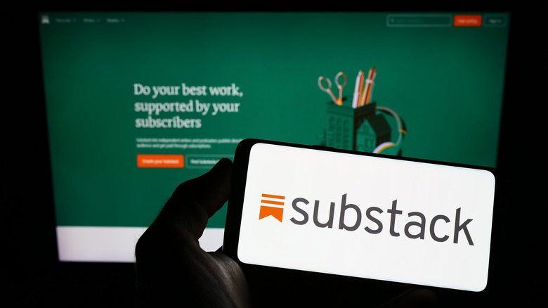 Substack logo on a smartphone held in front of a monitor