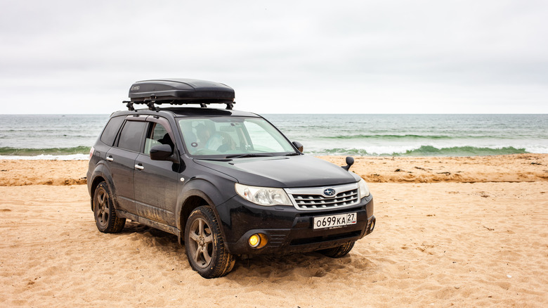 A black Subaru Forester on the beach, front 3/4 view