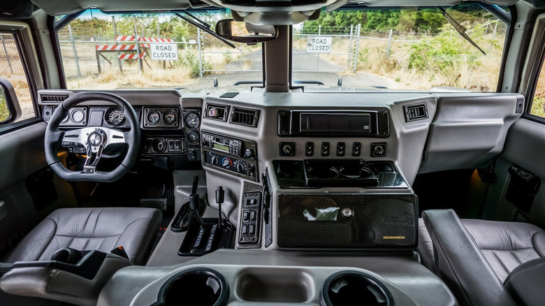 Interior of Hummer H1 showing steering wheel, dashboard and the large space between the drivers seat and passenger seat. Through the windshield a gate is visible displaying Road Closed signs.