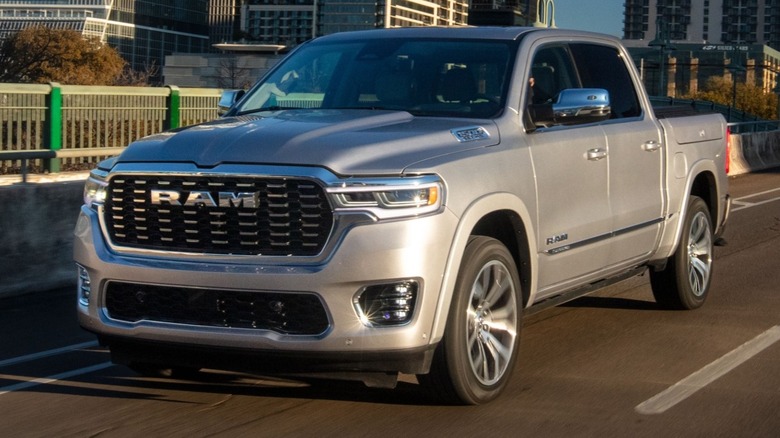 Silver 2025 Ram 1500 Tungsten driving down a city road with buildings in the background