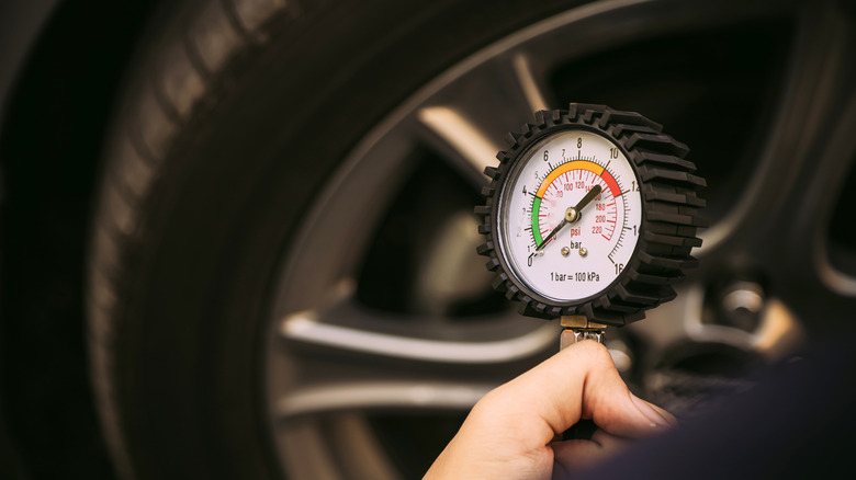 hand holding car tire pressure gauge near wheel