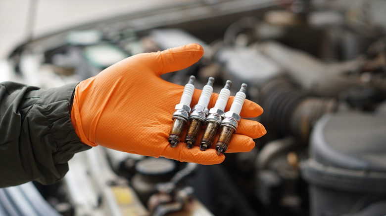 hand with orange glove holding four oil-fouled spark plugs