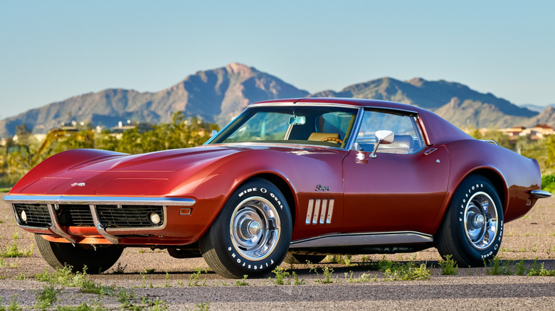 A red Corvette C3 in a field in front of mountains.