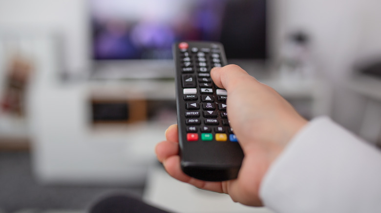 TV and using remote controller. Hand with remote controller changing channels or opening apps on smart TV