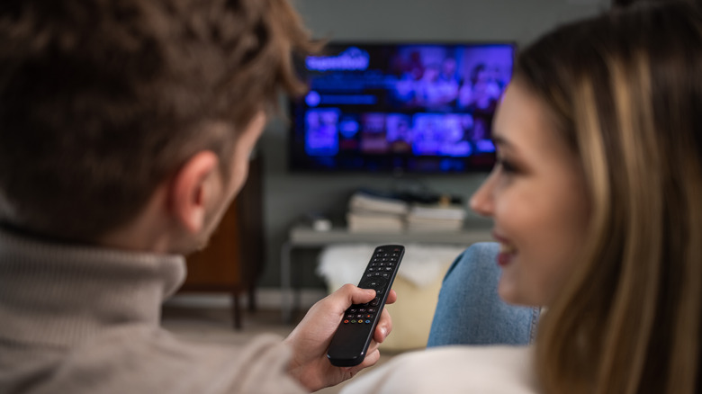 Rear view of cheerful couple smiling and talking while choosing a movie on TV