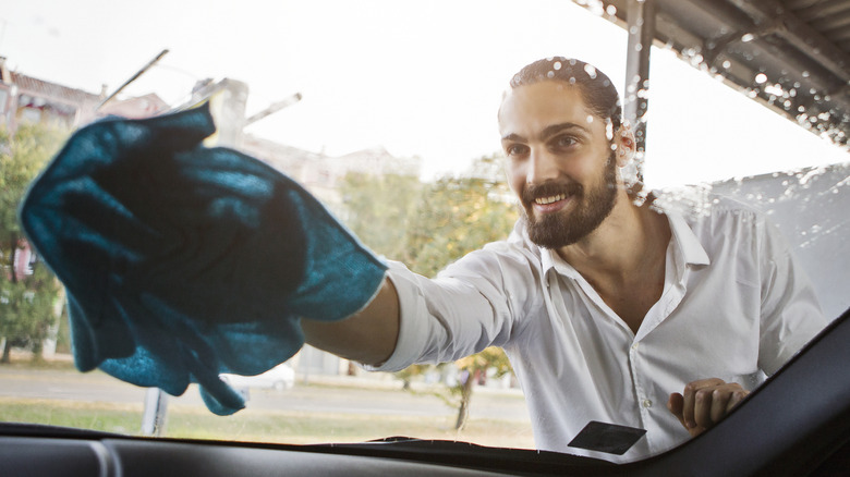 Smiling man washing his car winshield