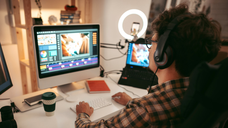 Man editing with headphones on at a white desk