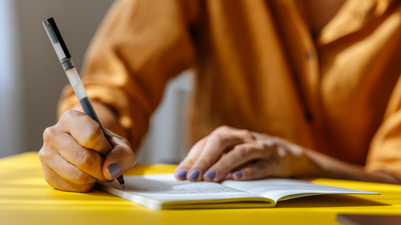 Person jotting down notes in notebook on yellow table