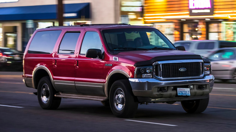 A two-tone red and gold Ford Excursion driving down the street, front 3/4 view