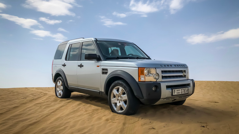 A Land Rover Discovery 3/LR3 in silver on a sand dune, front 3/4 view