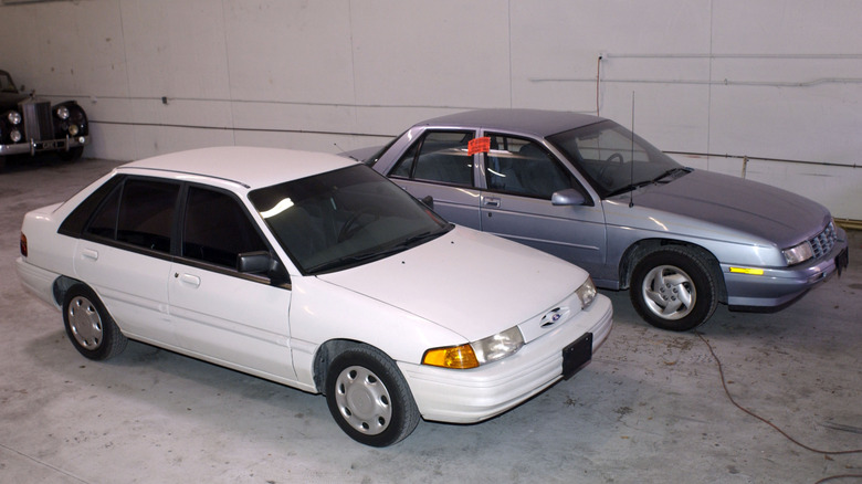 A white Ford Escort and faded-blue Chevrolet Corsica