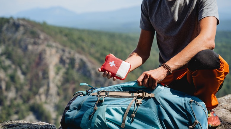 A man packing a small first aid kit into his backpack.