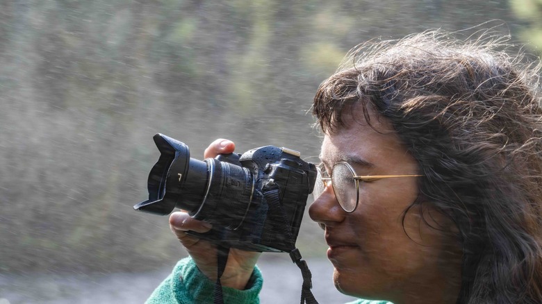 Woman taking a photo with the Om Systems OM-1 Mk II in blowing mist from a waterfall.