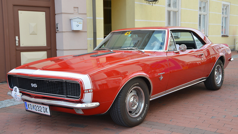 A 1967 first generation Chevrolet Camaro, front 3/4 view, red exterior with white stripes