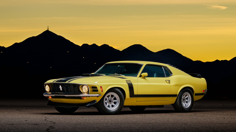 A 1970 Ford Mustang Boss 302, yellow with black stripes, front 3/4 view, sunset