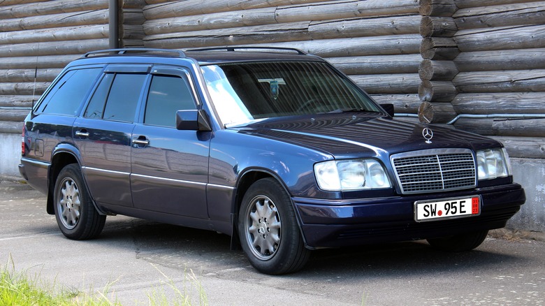 A black S124 Mercedes E-Class wagon on German export plates, front 3/4 view