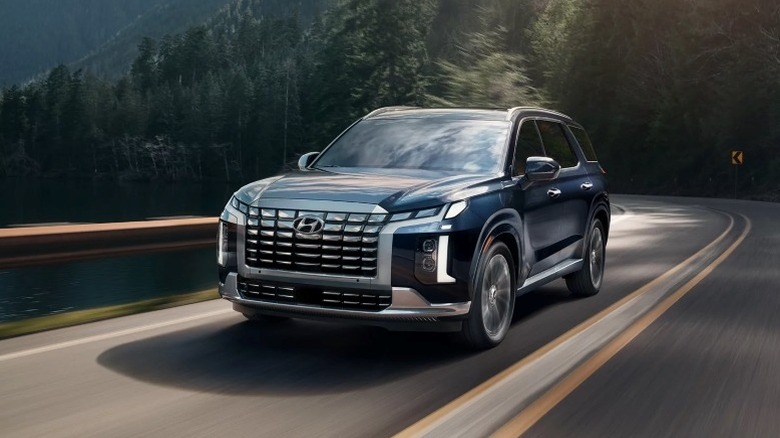 Blue Hyundai Palisade driving down a mountain road with trees in the background