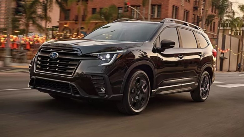 Black 2025 Subaru Ascent driving down a city street with buildings in the background