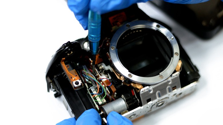 A DSLR camera being repaired on a white background.