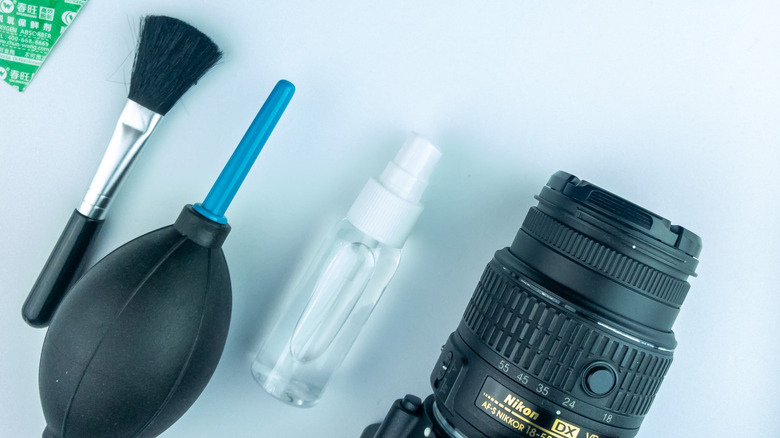 A brush, some liquid in a bottle, a DSLR camera and a manual air blower arranged to clean a sensor.