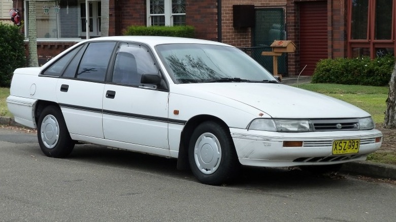 A white 1991-1992 Toyota Lexcen CSi sedan parked on the roadside in front of a building.