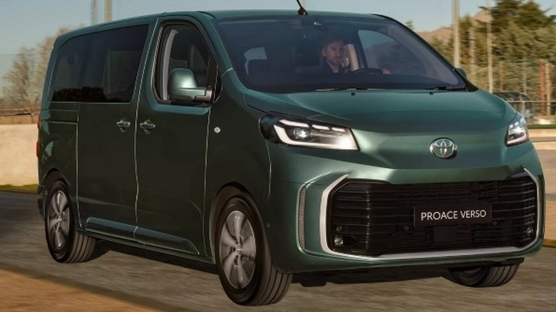 A forest green Toyota Proace Verso Electric driving on a road with trees in the background.