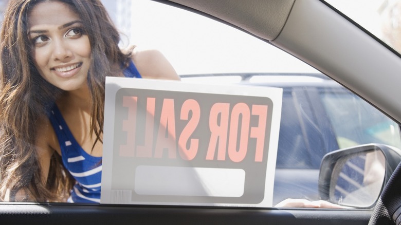 A woman peering into a car for sale