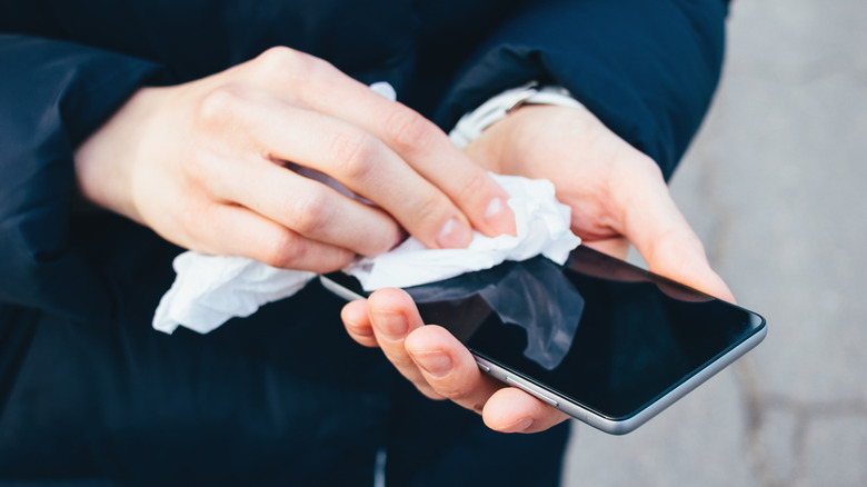 Person cleaning a smartphone with a disinfectant wipe.