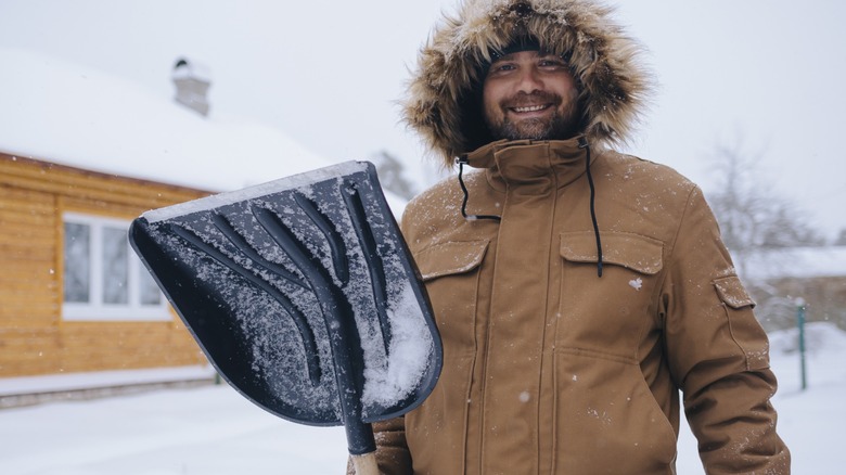 A man posing with a snow shovel.