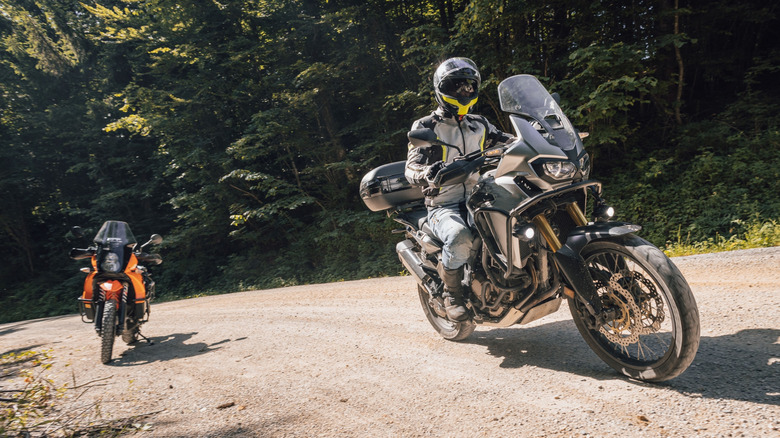 A pair of off-road motorcycles on a gravel path with a woodland background.