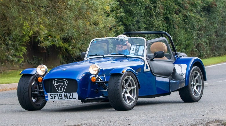 A person driving a blue Caterham Seven on road.