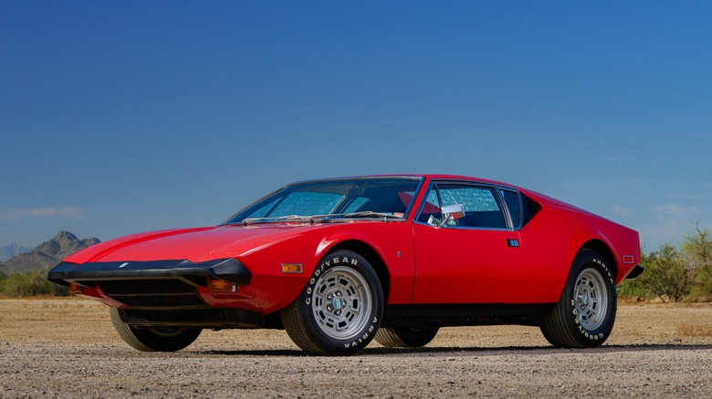 A DeTomaso Pantera in red parked outdoors on a gravel surface.