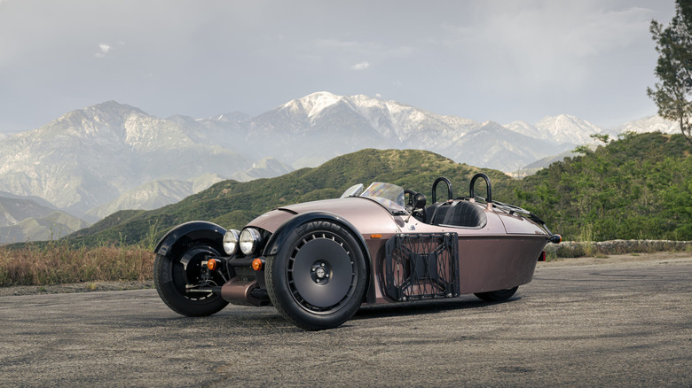 Morgan Super 3 in brown parked on a mountain road with a backdrop of snow-capped mountains.