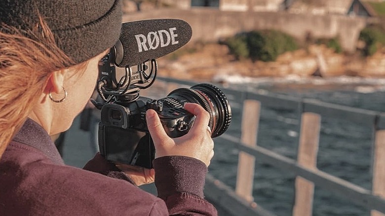 A woman filming with a Rode VideoMic Pro+ attached to her camera.