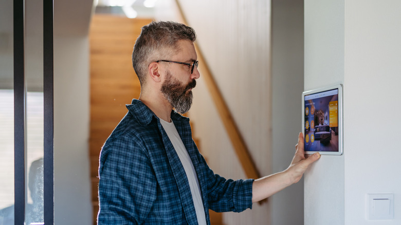 A man operating a smart home controller display mounted on a wall