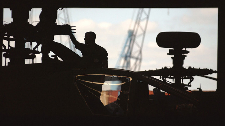 technicians silhouetted behind an AH-64 Apache