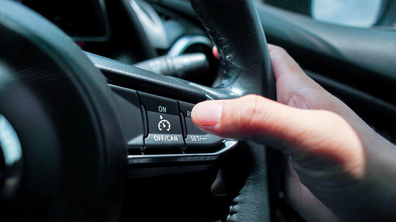 A hand activating cruise control on a car steering wheel.