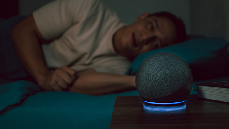 Man lying in bed and looking at Amazon Echo Dot on bedside table