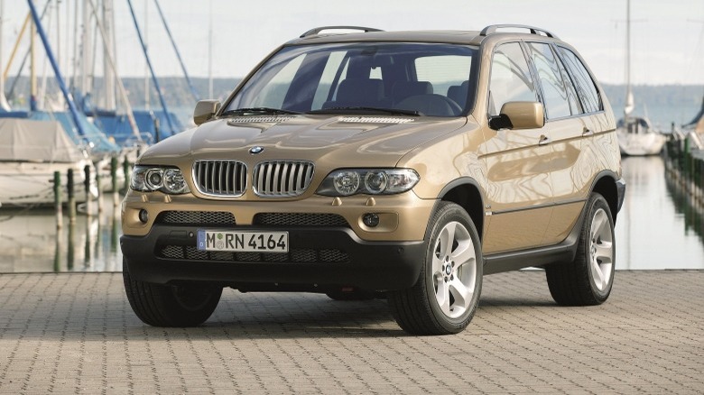 A gold-coloured X5 parked on a brick surface with a marina and boats in the background