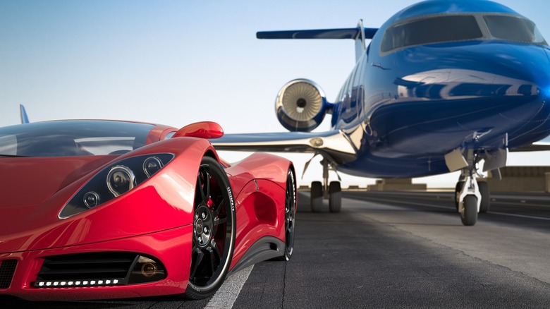 A red sports car parked beside a plane