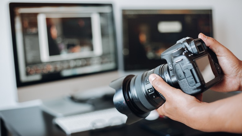 Person holding camera in front of computer