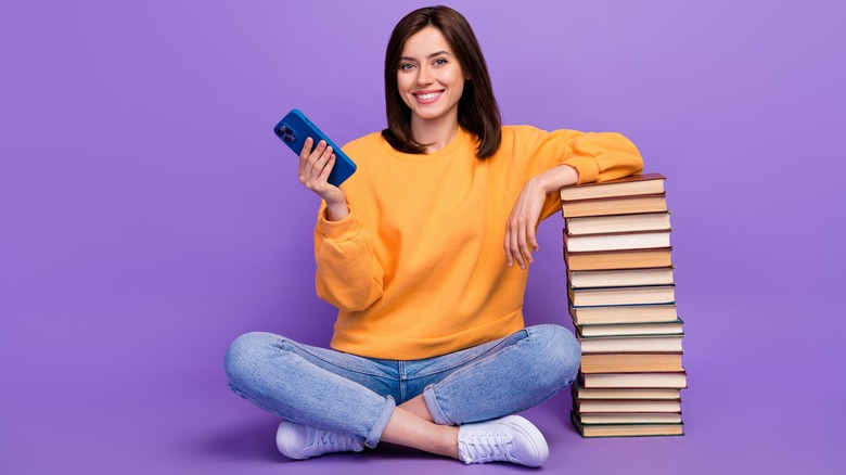 Woman with phone and stack of books