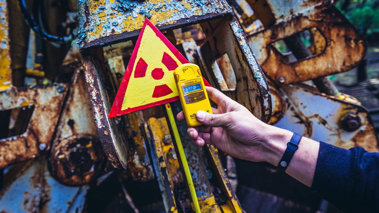 Man's hand holding a Geiger counter next to a radiation sign