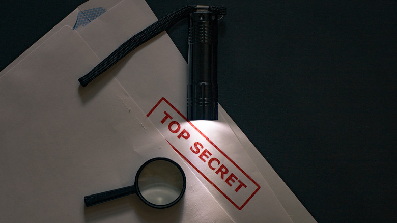 Opened envelope with Top Secret stamp, magnifying glass and flashlight 