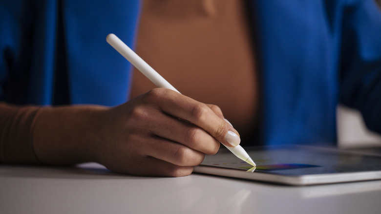 person using Apple Pencil on iPad wearing brown shirt and blue jacket