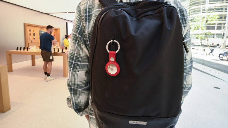 A man in plaid shirt wearing a black knapsack with an AirTag in one zipper