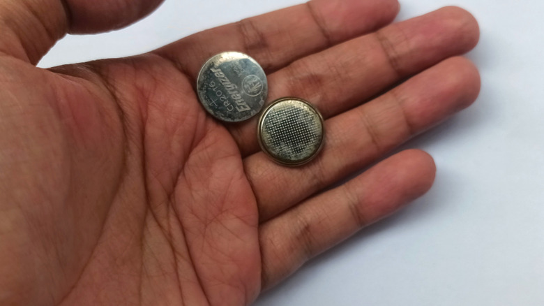 A hand holding two coin cell batteries